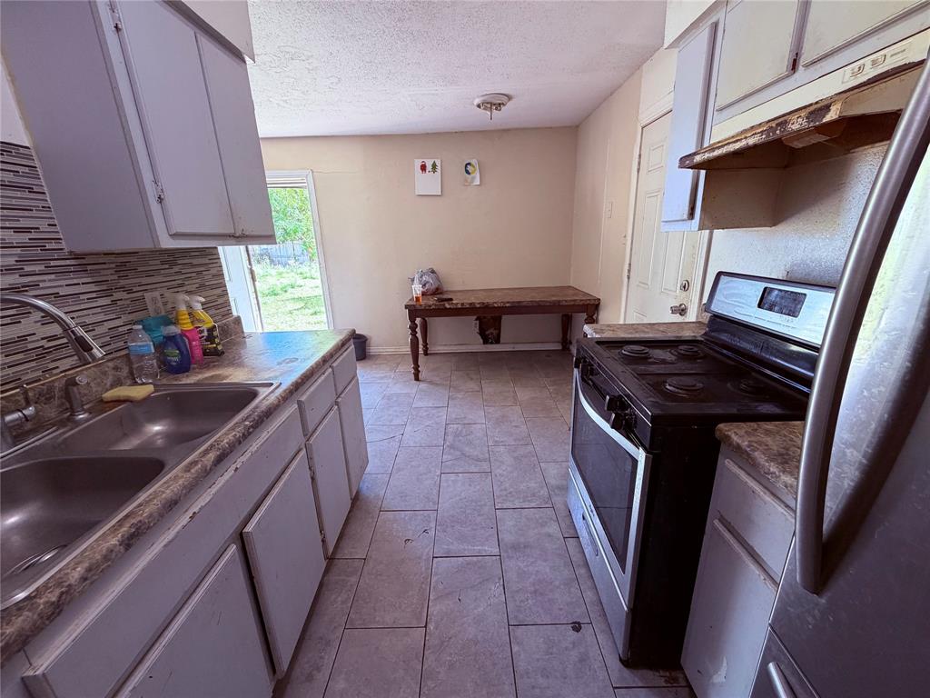 Kitchen featuring tile flooring, stone-patterned laminate countertops, stainless steel double-basin sink with gooseneck faucet, tiled backsplash, and light-toned cabinetry