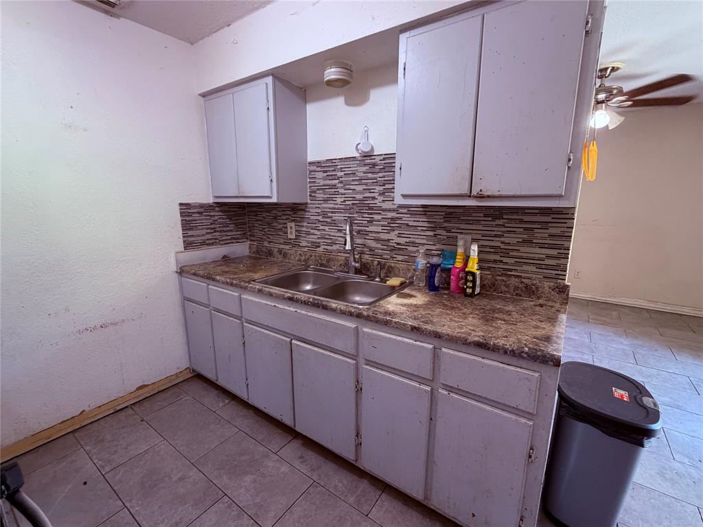 Kitchen area featuring custom cabinetry, laminate countertops, a dual-basin stainless steel sink, and decorative mosaic tile backsplash