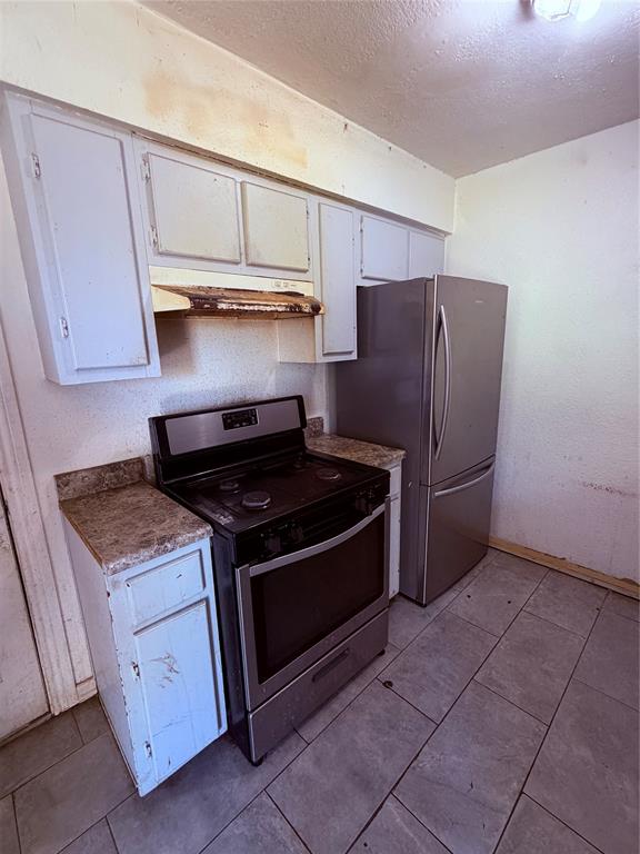Kitchen featuring shaker-style cabinetry, stone-finish countertops, stainless steel appliances, and tile flooring