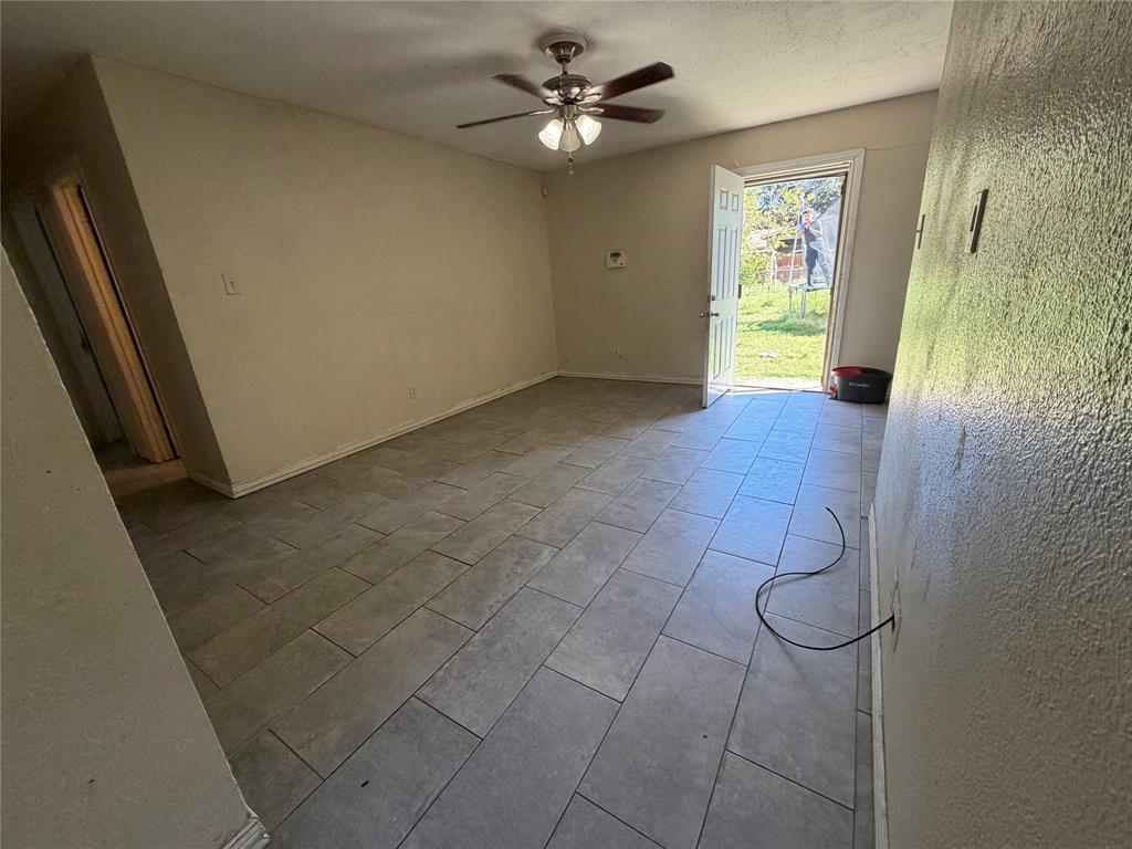 Interior space featuring large-format tile flooring, a ceiling fan with integrated lighting, and a single-pane glass-panel exterior door