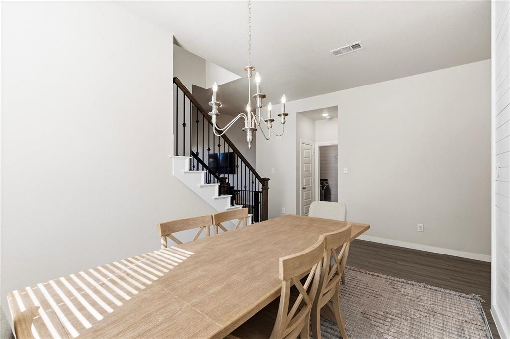 Staircase featuring a dark wood-finish handrail and black metal balusters, illuminated by a multi-arm candle-style chandelier over wood-finish flooring