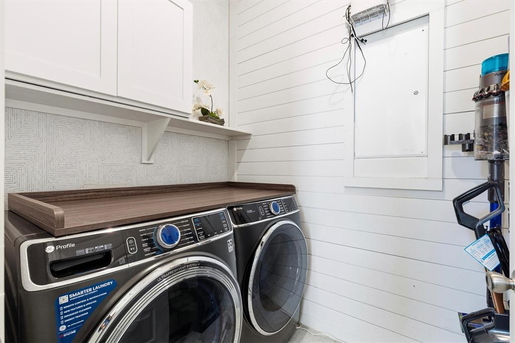Laundry area featuring shiplap wall paneling, white shaker-style cabinetry, a wood-finish folding counter, and patterned wallpaper