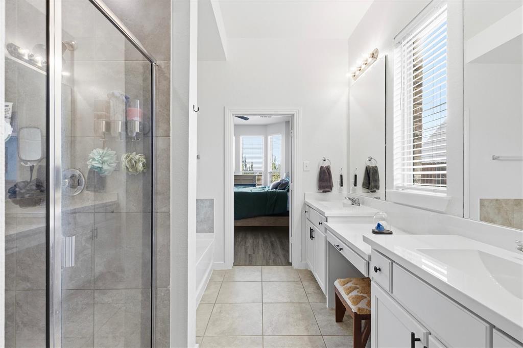 Bathroom featuring a dual-sink vanity with white cabinetry, quartz countertops, a glass-enclosed shower with tile surround, and large-format tile flooring