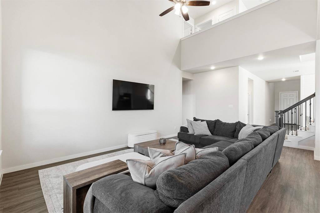 Double-height ceilings, wood-finish flooring, recessed lighting, ceiling fan, and a staircase with iron balusters