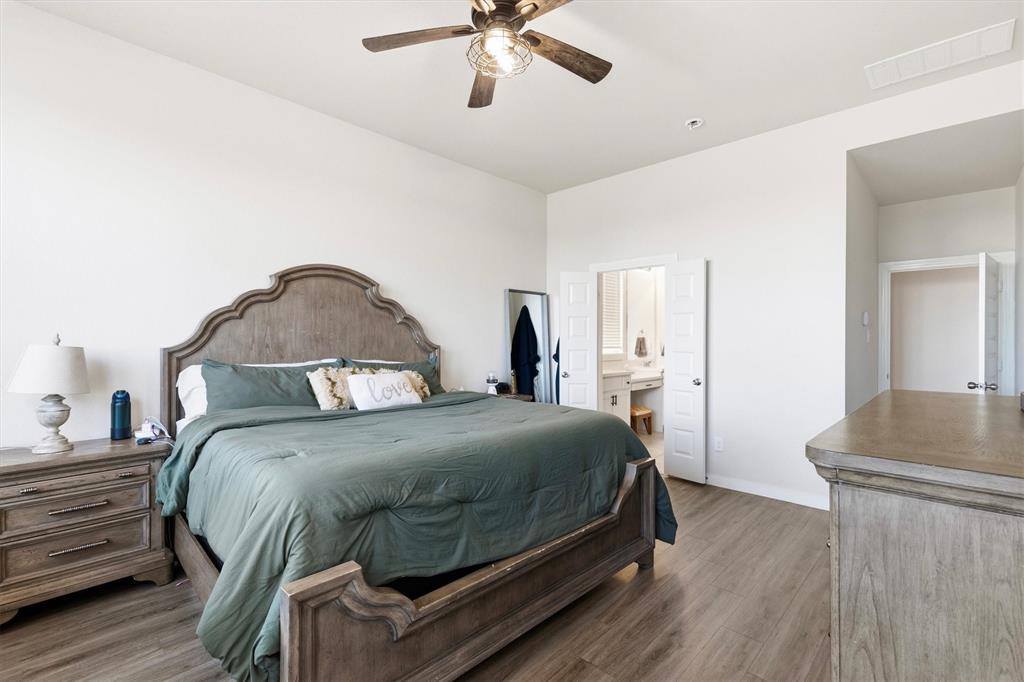 Spacious room featuring wood-finish flooring, a central ceiling fan with an integrated light fixture, and double doors opening to a secondary room