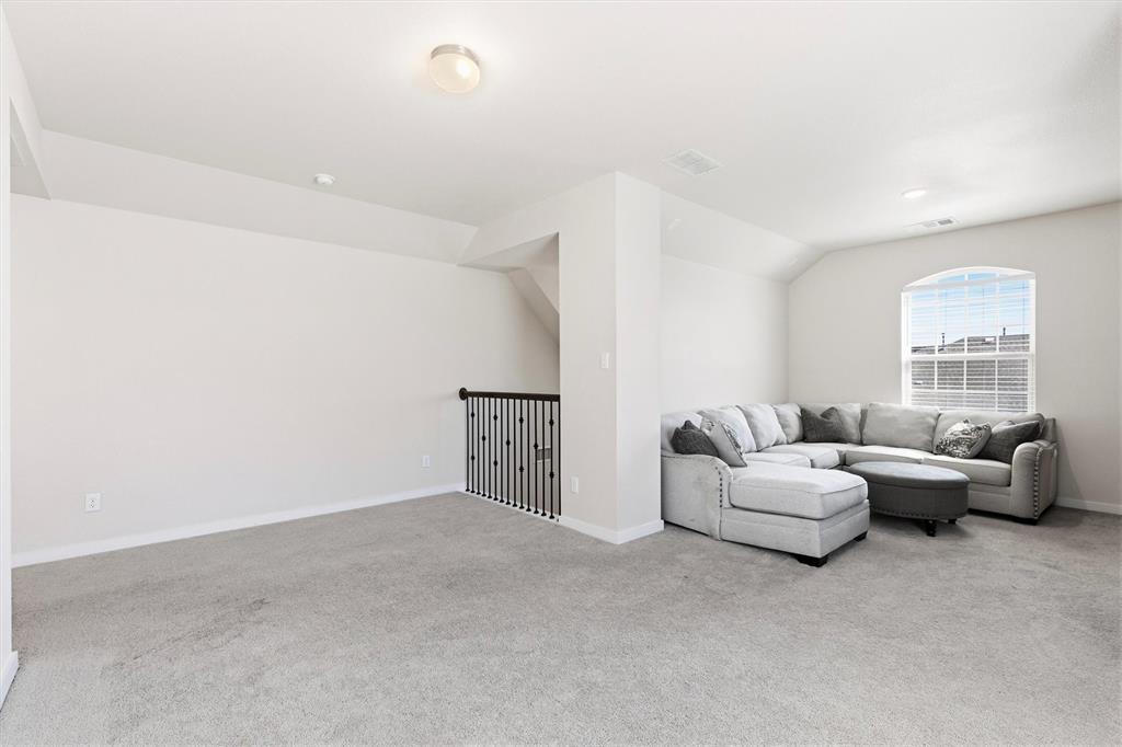 Open room featuring neutral carpeting, arched window, and metal baluster railing
