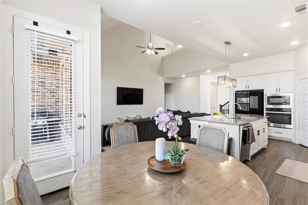 Kitchen featuring a central island with a stainless steel sink, built-in double oven, white cabinetry with matte black hardware, recessed lighting, and wood-finish flooring