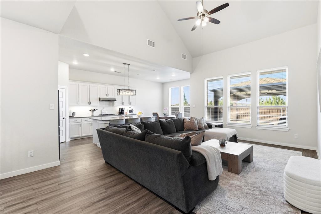 Vaulted ceilings, wood-finish flooring, white cabinetry, kitchen island with pendant lighting, and abundant natural light from tall windows