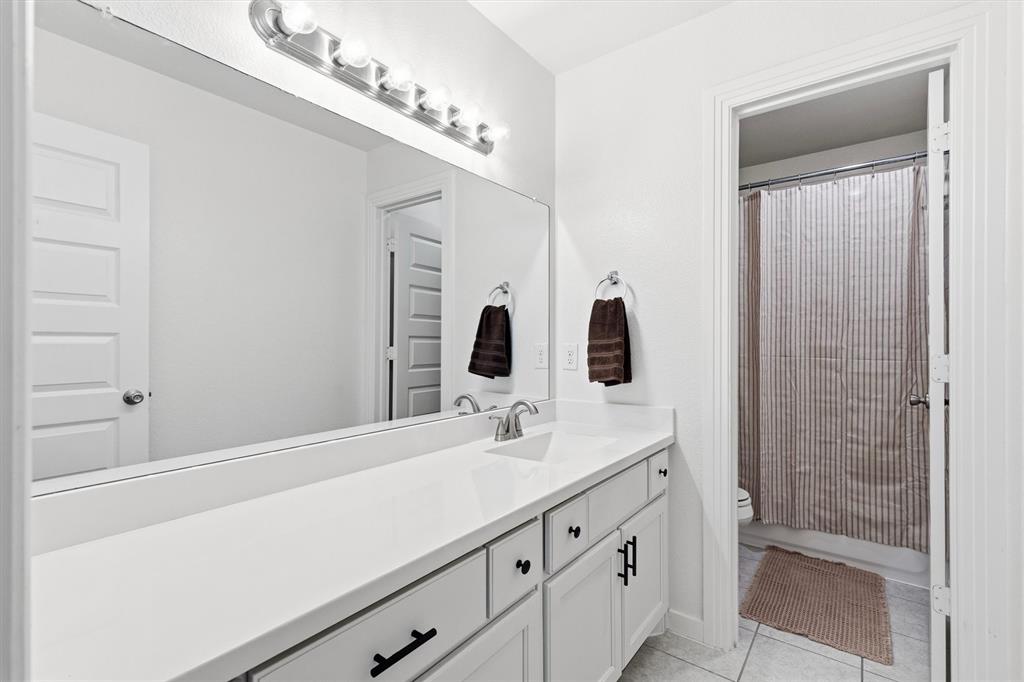 Bathroom vanity featuring white shaker-style cabinetry, matte black hardware, a solid surface countertop with an integrated sink, a full-width wall mirror, and a multi-bulb light fixture