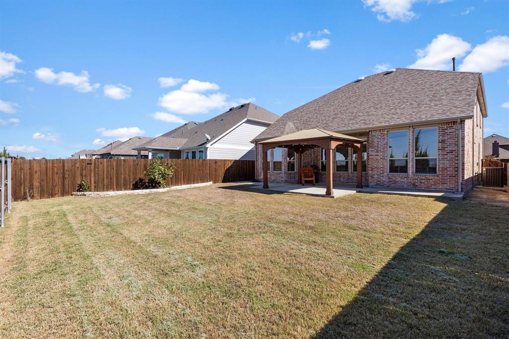 Rear exterior featuring brick masonry, a covered patio area, and a wood privacy fence enclosing the lawn