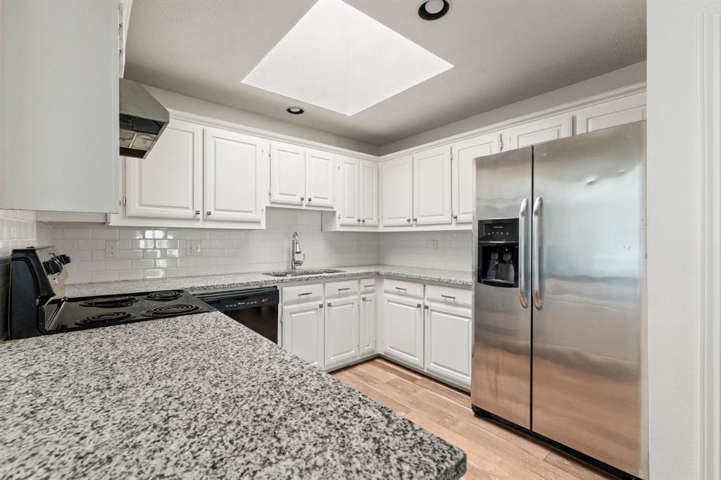 Kitchen featuring white shaker-style cabinetry, stone-finish countertops, subway tile backsplash, stainless steel appliances, and a ceiling skylight