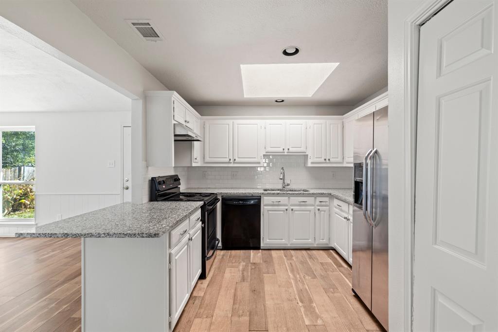 Kitchen featuring white cabinetry, stone-finish countertops, subway tile backsplash, wood-finish flooring, and a ceiling skylight