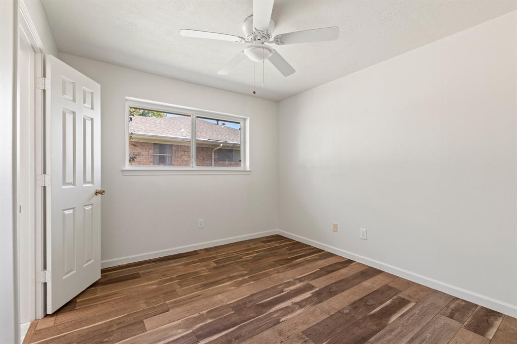 Room featuring wood-finish flooring, a white-paneled interior door, and a ceiling-mounted fan with integrated lighting