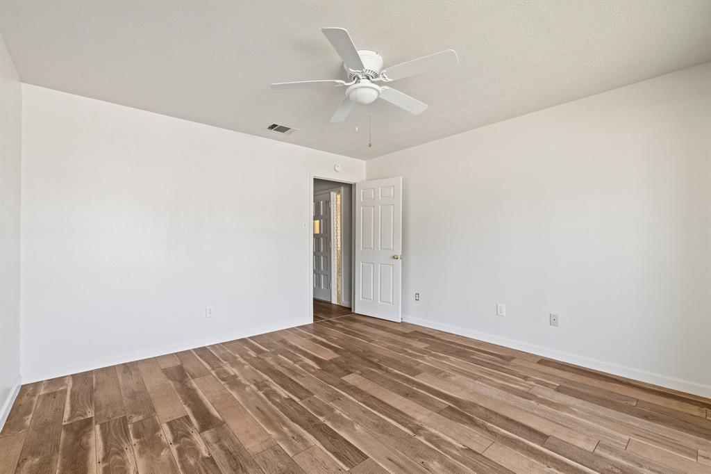 Interior room featuring wood-finish flooring, white walls, and a ceiling-mounted fan with integrated lighting