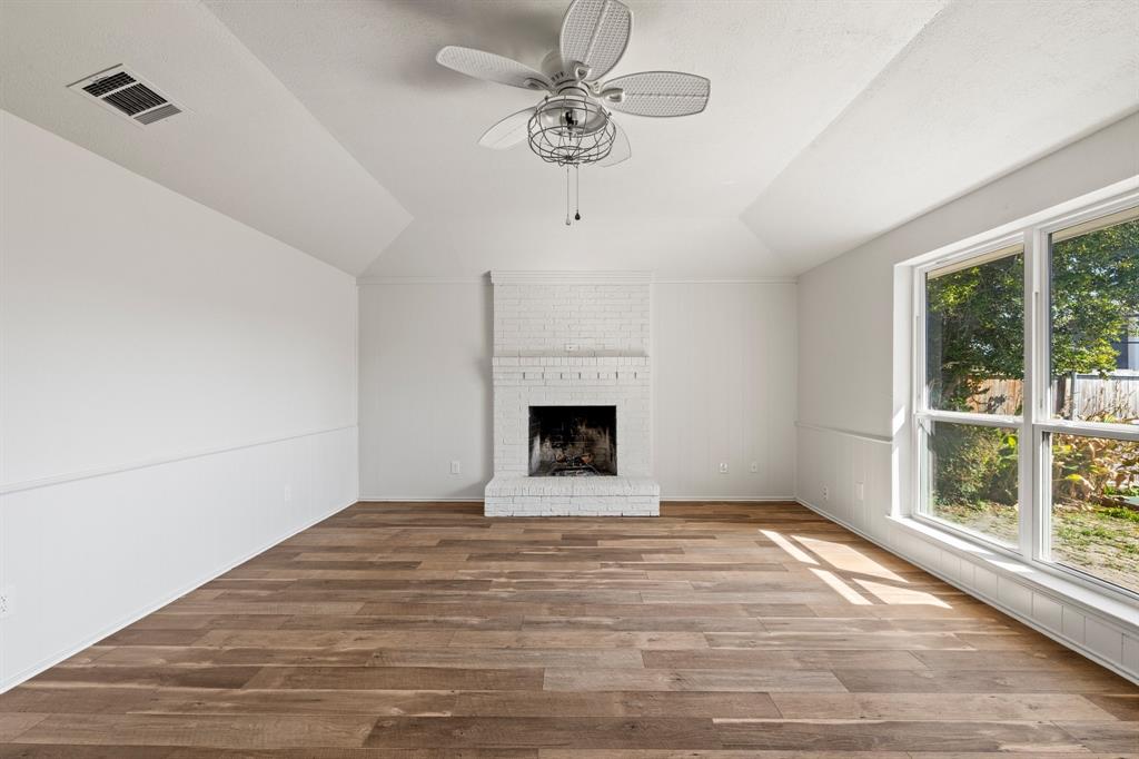 Vaulted ceiling, white-painted brick fireplace, wood-finish flooring, and large window with exterior natural light Vaulted ceiling, white-painted brick fireplace, wood-finish flooring, and large window with exterior natural light