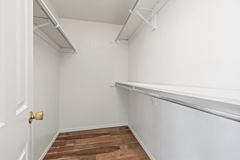 Storage space featuring wood-finish flooring, metal hanging rods, and built-in shelving