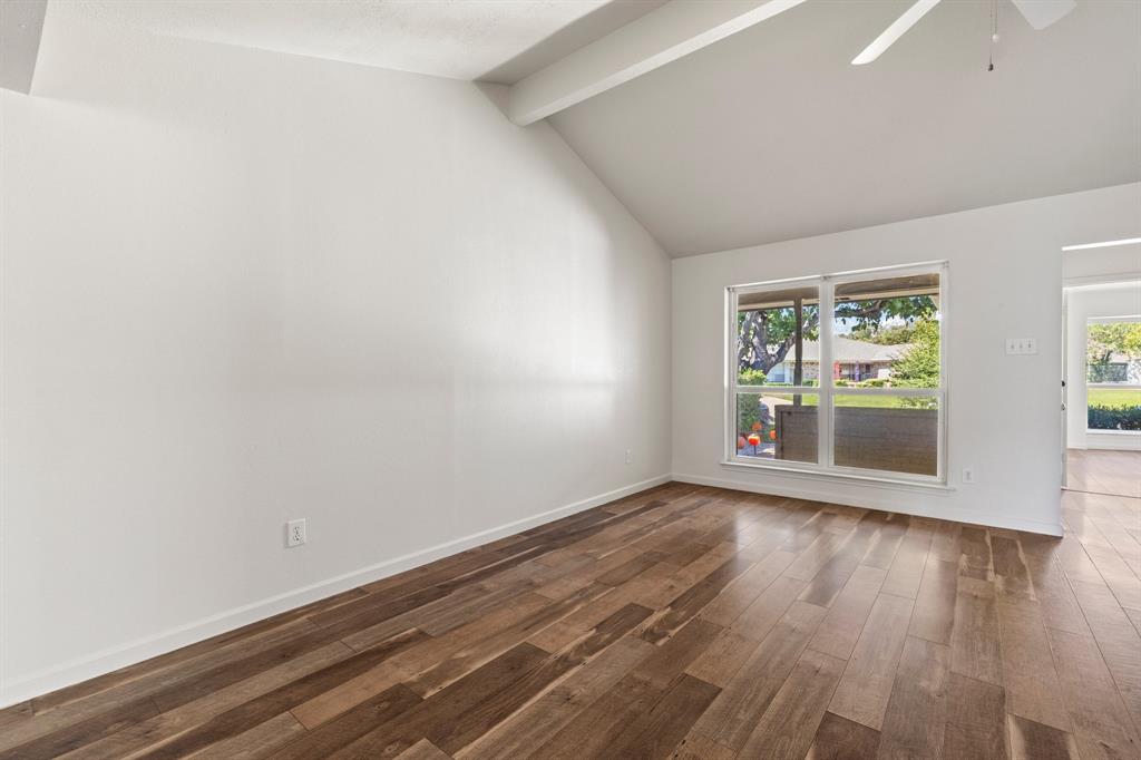 Vaulted ceiling featuring exposed beams, wood-finish flooring, and a multi-pane window