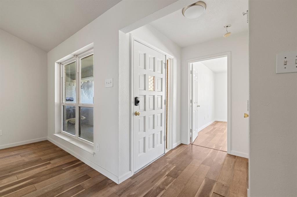 Interior featuring wood-finish flooring, white walls, paneled exterior entry door, and multi-pane window Interior featuring wood-finish flooring, white walls, paneled exterior entry door, and multi-pane window