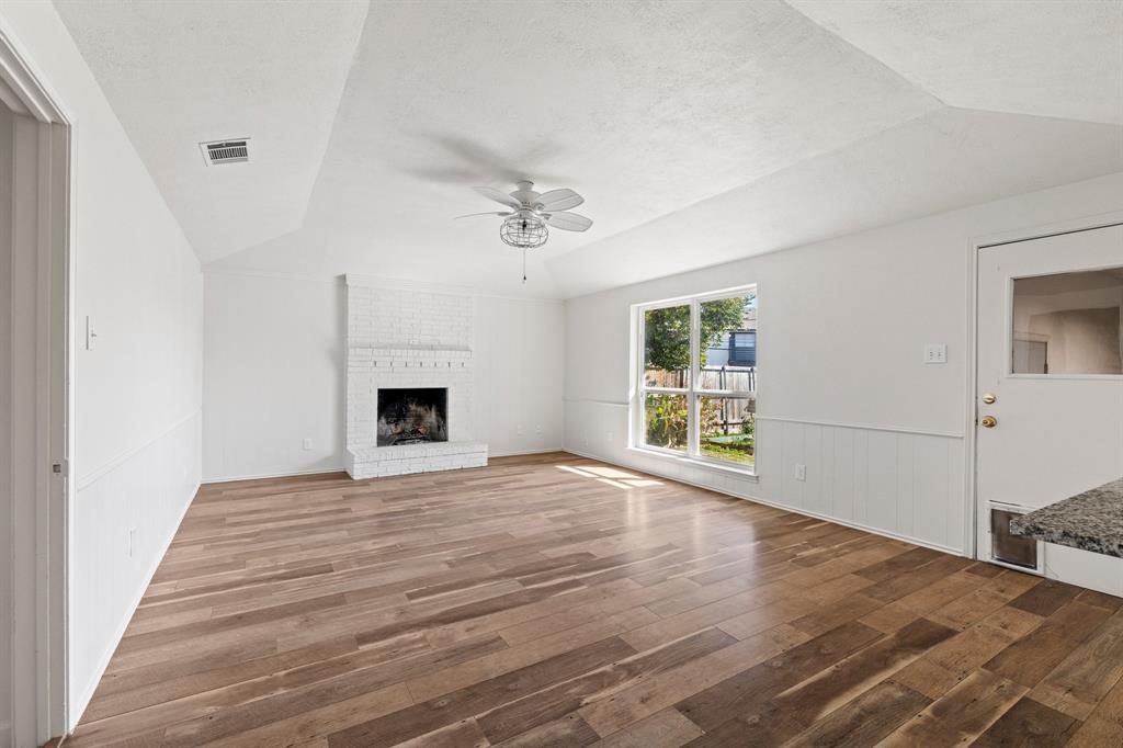 Vaulted ceilings, wood-finish flooring, white painted brick fireplace, large picture window, and wainscoting