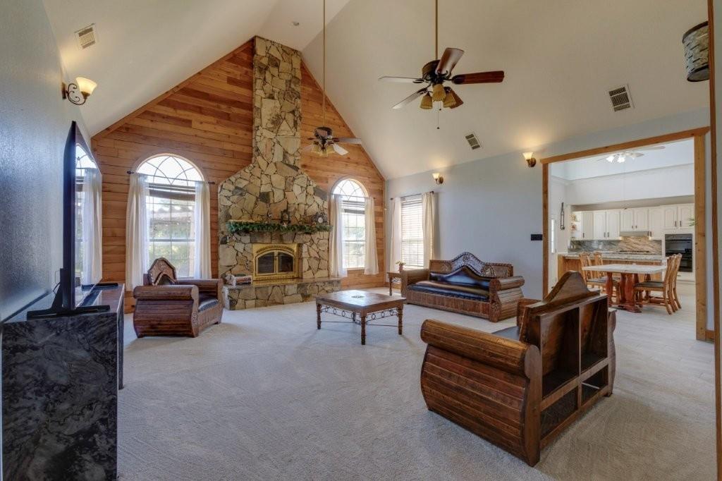 Vaulted ceiling featuring wooden accent wall, floor-to-ceiling stone fireplace with mantel, and arched windows