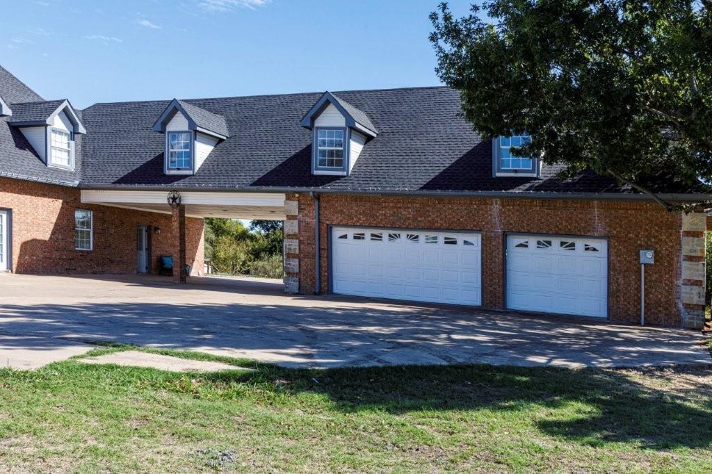 Brick exterior featuring a multi-car garage, dormer windows, asphalt shingle roofing, and a covered porte-cochere