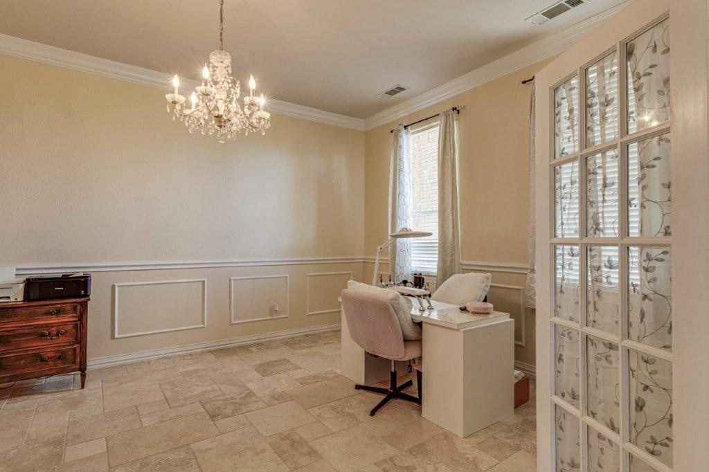 Room featuring large-format stone-style tile flooring, decorative wall molding, crown molding, and an ornate multi-arm crystal chandelier, accessed via a multi-lite glass French door