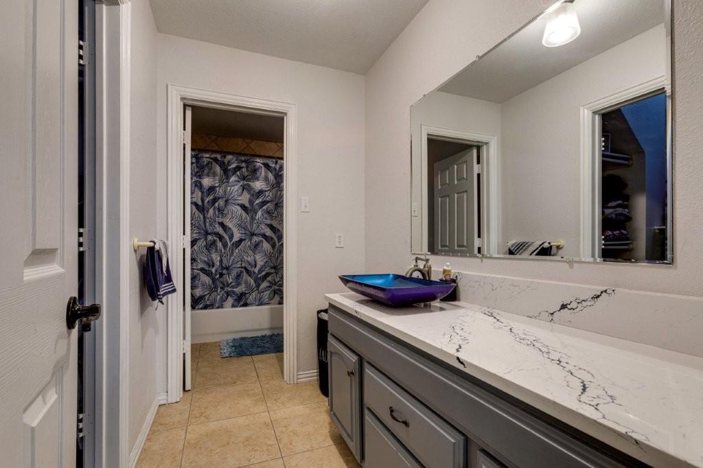Bathroom vanity featuring a quartz-style countertop, integrated blue glass vessel sink, gray shaker-style cabinetry, and a large wall-mounted mirror
