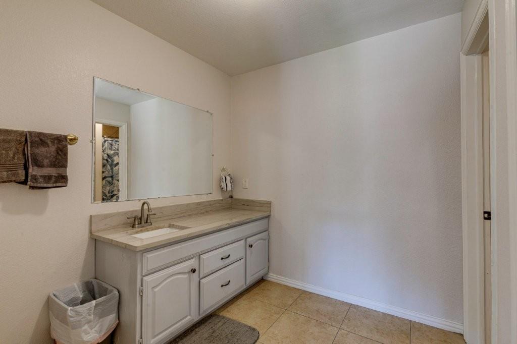 Built-in vanity featuring a stone-look countertop, integrated sink, large wall-mounted mirror, and ceramic tile flooring