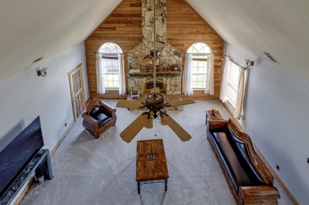 Vaulted ceiling with wood-paneled feature wall, floor-to-ceiling stone fireplace, and arched windows