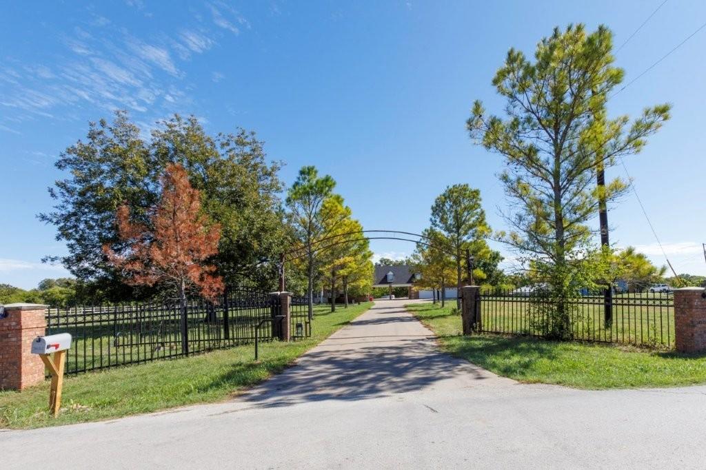 Gated entrance featuring decorative iron fencing, brick masonry pillars, and a paved driveway lined with mature trees