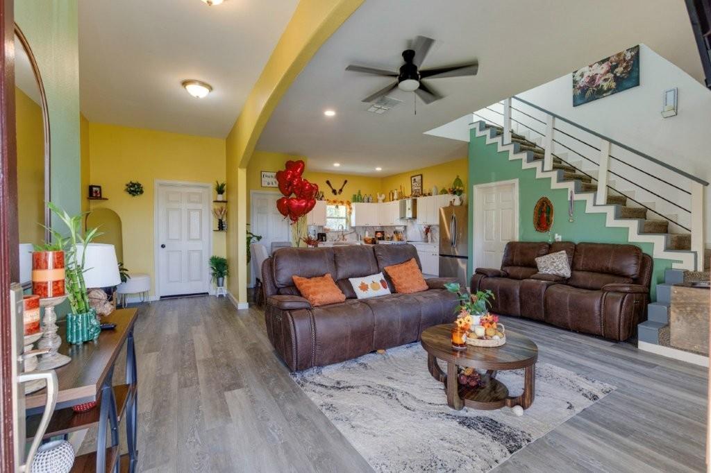 Open-concept living space featuring wood-finish flooring, recessed lighting, ceiling fan, and a staircase with metal railing