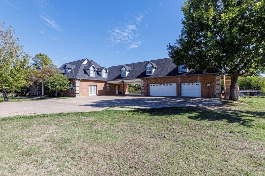 Brick exterior with multi-gabled roofline, dormer windows, attached two-car garage, and expansive concrete motor court