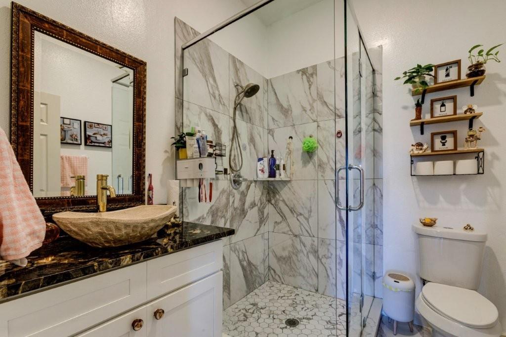 Bathroom featuring a vessel sink with a gold-finish faucet, dark stone countertop, white shaker-style cabinetry, and a frameless glass-enclosed shower with large-format wall tile and hexagonal floor tile