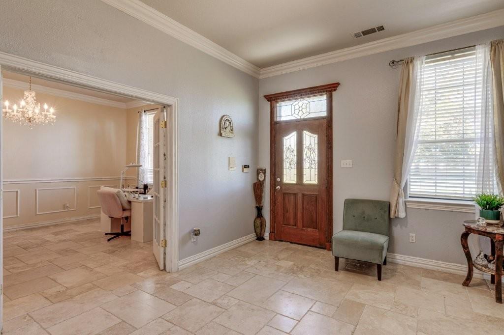 Entryway featuring natural stone tile flooring, a solid wood entry door with stained glass accents, decorative transom window, and crown molding