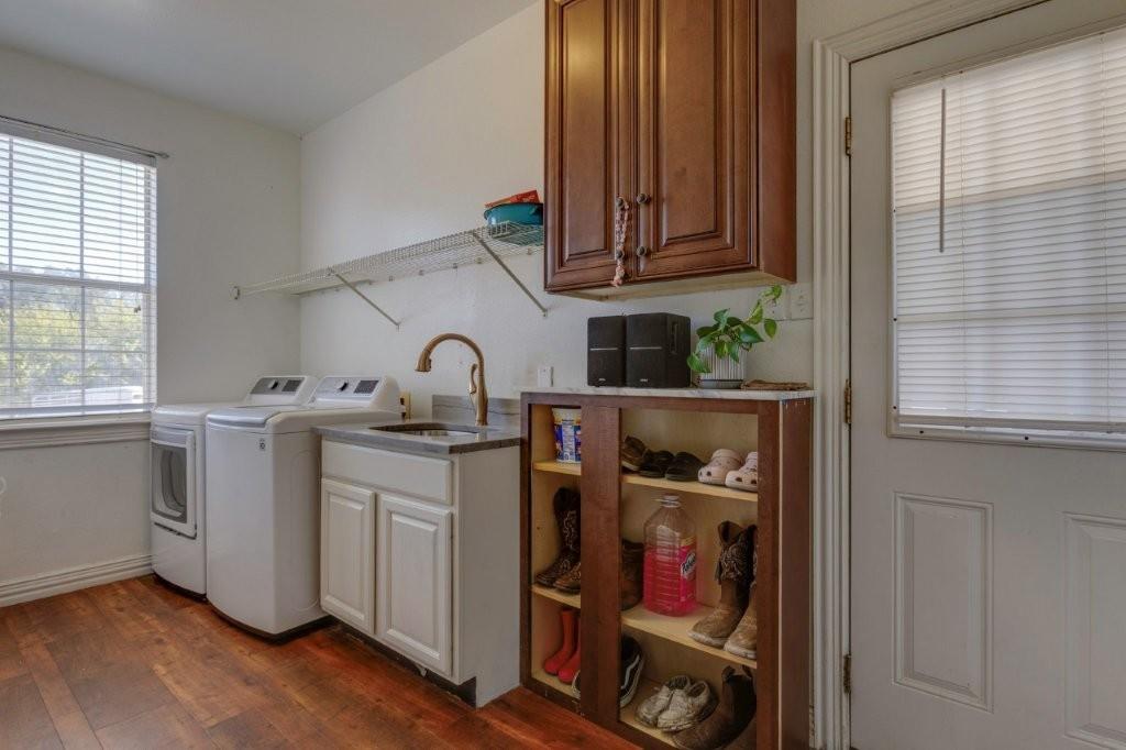 Laundry area featuring wood-finish flooring, a built-in utility sink with a high-arch faucet, custom wood cabinetry, and an open-shelf storage unit