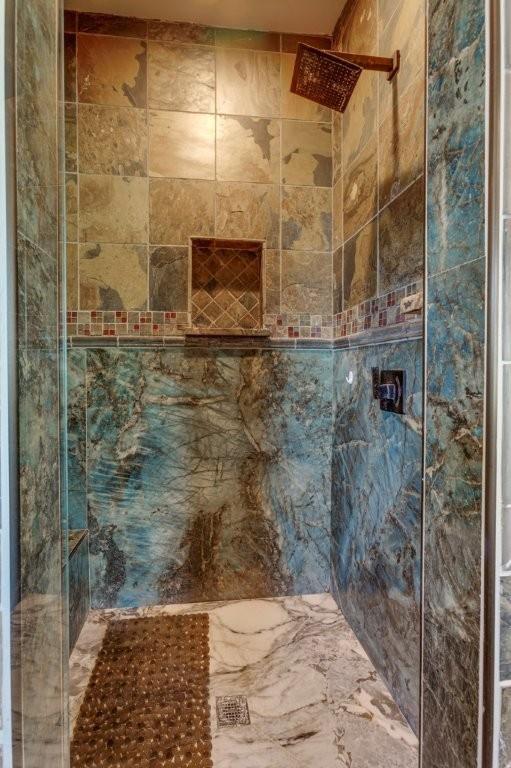 Walk-in shower featuring large-format natural stone wall tile, an inset wall niche, a glass enclosure, and a metallic rain showerhead