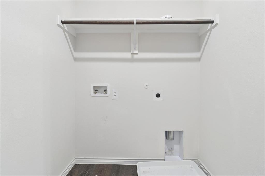 Utility area featuring wood-finish flooring, white walls, and an overhead shelf with an integrated hanging rod