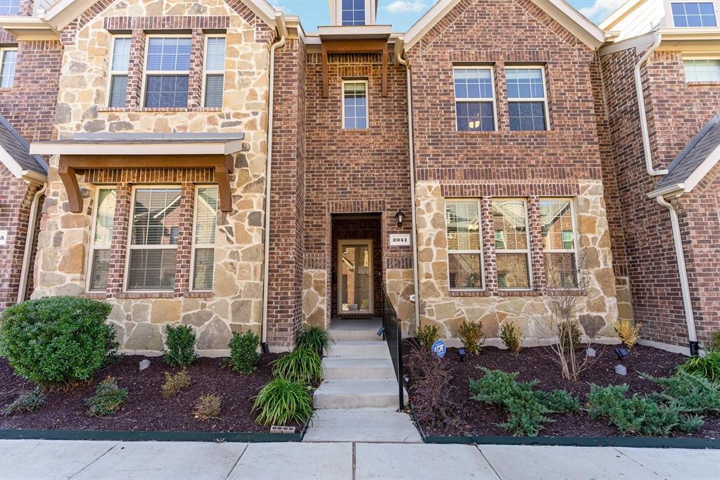 Exterior facade featuring a mix of brick and stone masonry, multi-pane windows, wood-bracketed roof accents, and concrete stairs leading to a recessed entryway