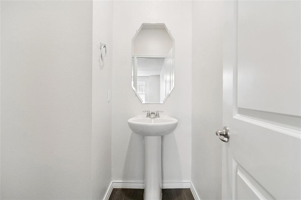 Pedestal sink with chrome dual-handle faucet, octagonal wall-mounted mirror, and wood-finish flooring
