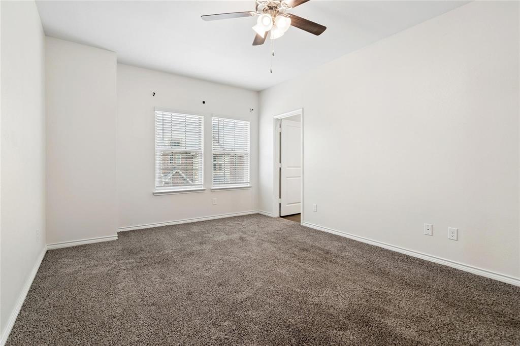Neutral-toned carpeting, dual windows with horizontal blinds, and a ceiling-mounted fan with integrated lighting