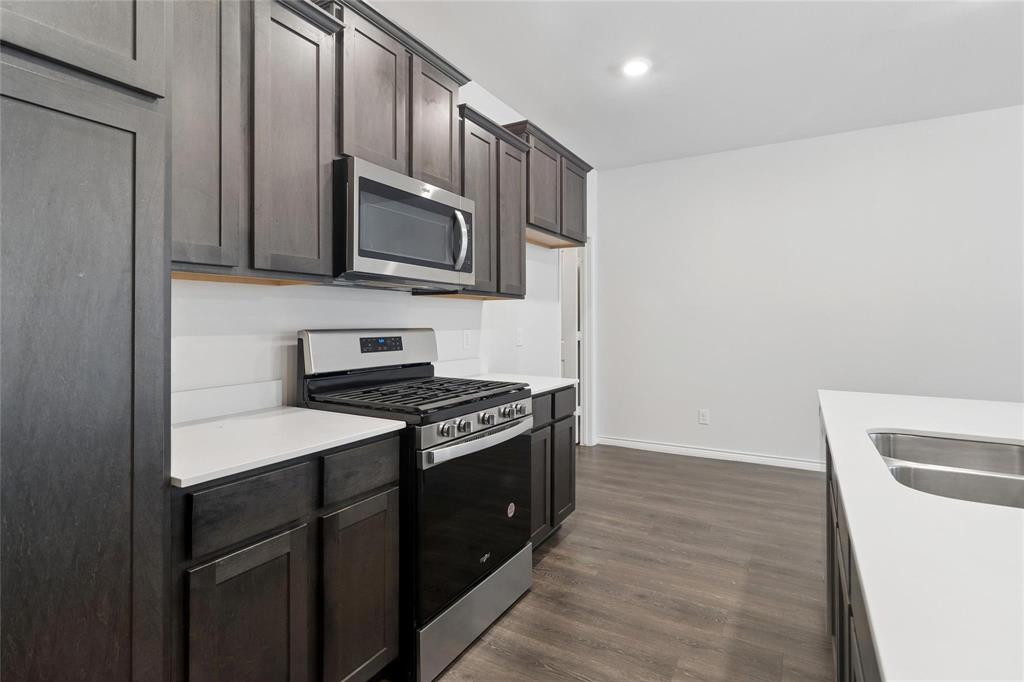 Kitchen featuring dark-finish cabinetry, quartz countertops, stainless steel gas range, built-in microwave, and wood-finish flooring Kitchen featuring dark-finish cabinetry, quartz countertops, stainless steel gas range, built-in microwave, and wood-finish flooring