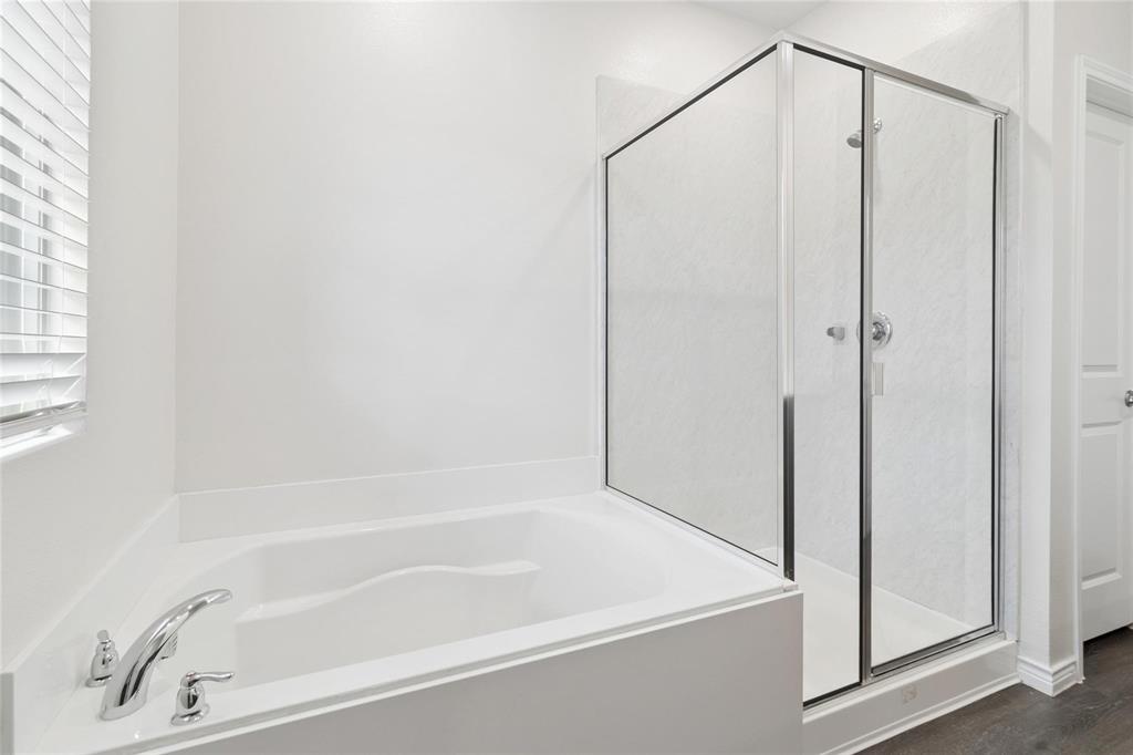 Soaking tub with chrome faucet fixture, glass-enclosed shower, and wood-finish flooring