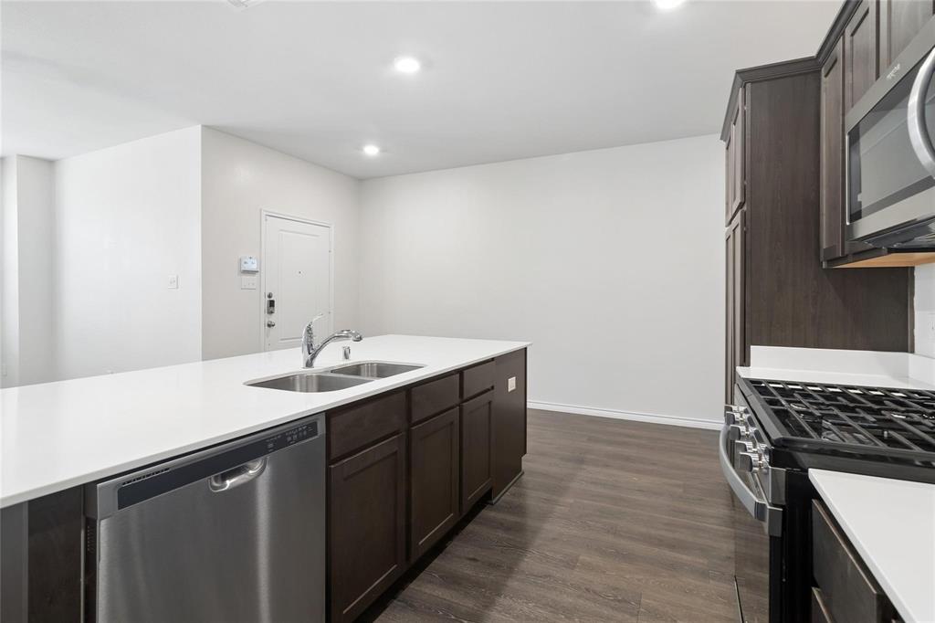 Kitchen featuring dark-finish cabinetry, white countertops, stainless steel dual-basin sink, gas range, and wood-finish flooring
