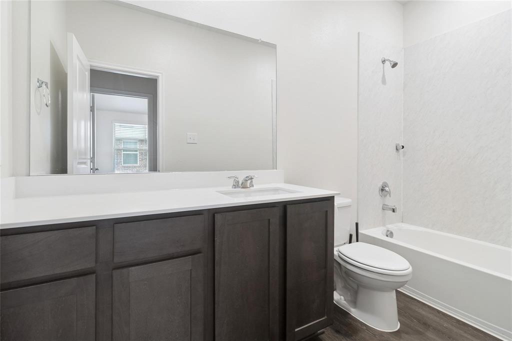 Bathroom featuring a dark-finish vanity with a white countertop, an integrated sink, a large wall-mounted mirror, and a tub-shower combination with a textured surround
