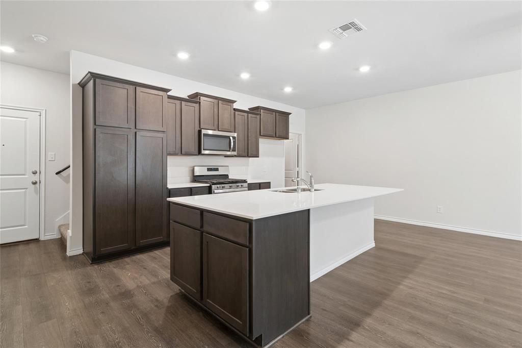 Kitchen featuring dark wood-finish cabinetry, a white countertop island, stainless steel microwave, gas range, and wood-finish flooring