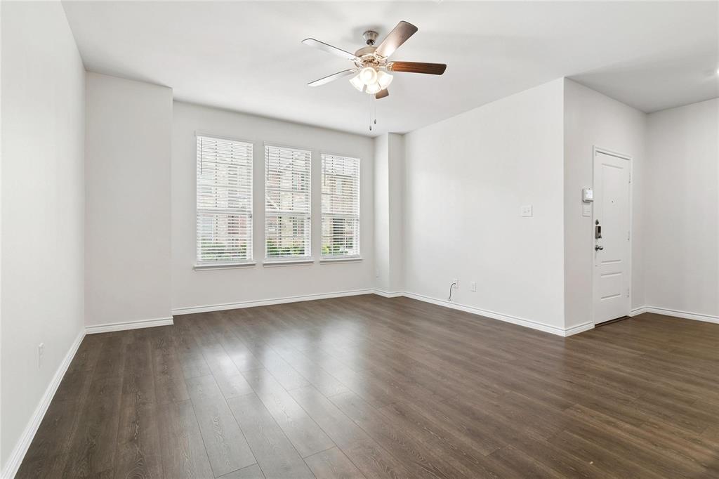 Living space featuring wood-finish flooring, a multi-blade ceiling fan with integrated lighting, and three tall windows with horizontal blinds