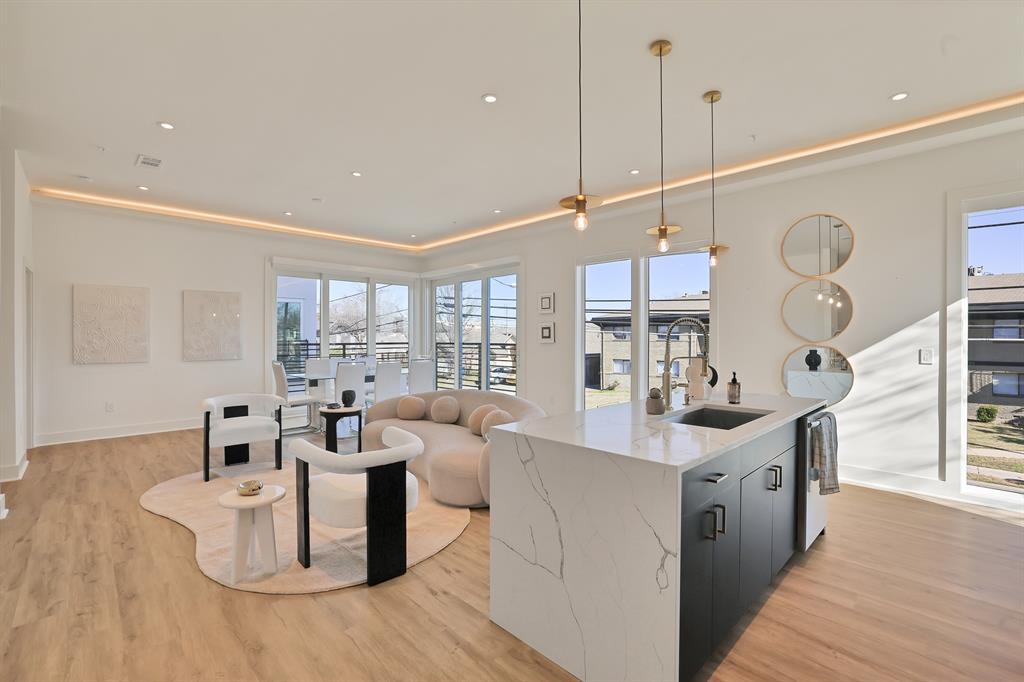 Kitchen with sink, light hardwood / wood-style flooring, light stone countertops, an island with sink, and decorative light fixtures