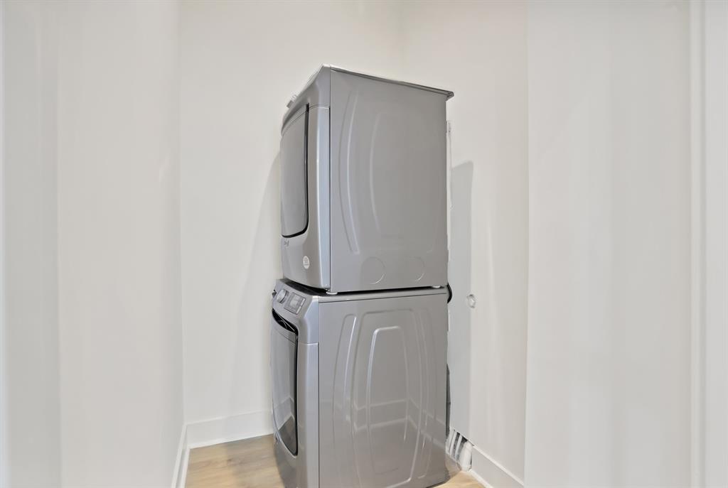Clothes washing area with stacked washing maching and dryer and light hardwood / wood-style floors
