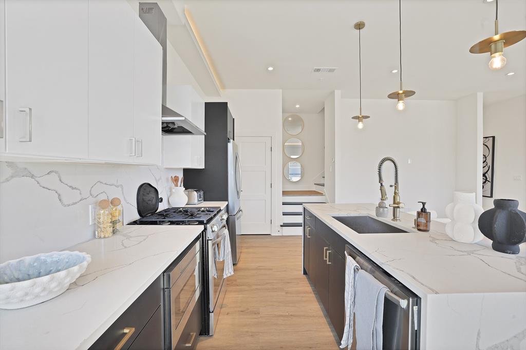 Kitchen featuring decorative light fixtures, white cabinetry, sink, light stone counters, and stainless steel appliances