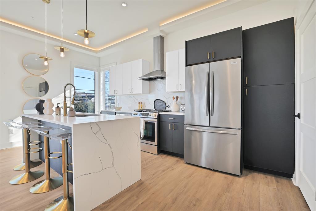 Kitchen with appliances with stainless steel finishes, decorative light fixtures, tasteful backsplash, white cabinetry, and wall chimney exhaust hood